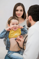 Pediatrician doctor examining kid boy. Mother holding baby.