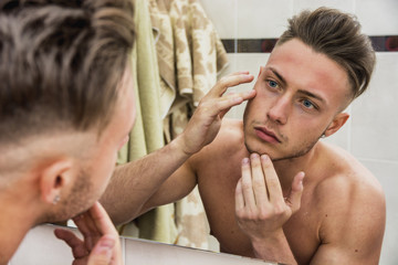 Young man touching his face while looking in mirror