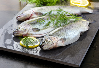 Raw rainbow trouts on a stone board with herbs and lemon, ready for cooking
