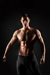 Obraz na płótnie Canvas Sexy shirtless bodybuilder posing, looking at camera on black ba