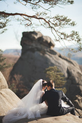 Gorgeous wedding couple kissing and hugging in forest with big rocks