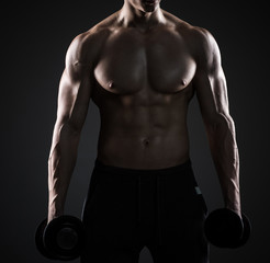 Fototapeta na wymiar Muscular man showing perfect body with dumbbells on black background