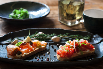 Sandwiches with smoked salmon and tomato on black plate close up. Focus on foreground. Bruschetta with seafood and tomatos, served on wooden background