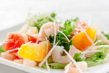 Fresh yummy shrimp salad with oranges and grapefruit  and cheese on the white dish. Close up. Top view of seafood salad with shrimp
