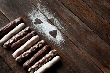 Dark wooden table decorated with sugar powder hearts and chocolate candies. Top view, free space. White, dark and decorated chocolate cake sticks closeup. Advertising confectionery
