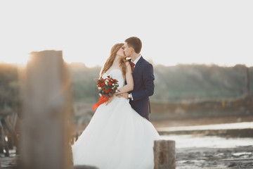 Fototapeta na wymiar Wedding couple, groom, bride with bouquet posing near sea on sunset