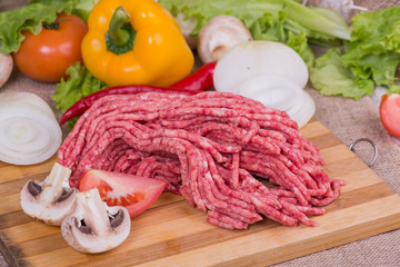 fresh raw mince  meat on a chopping board with vegetables and greens