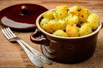 Roasted young potatoes with garlic and dill on brown wooden background.