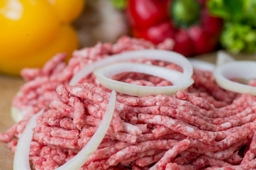 Raw minced meat and onion rings close-up with fresh vegetables on the background