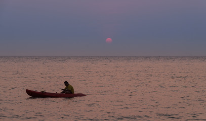 Silhouette of a man rowing in the canoe at sunset 