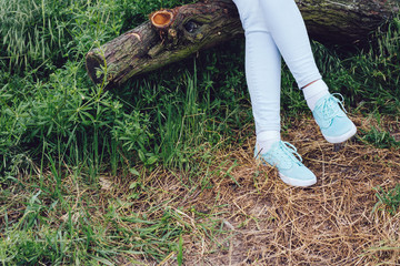 Fototapeta premium Female feet in sneakers and jeans on a log in the forest