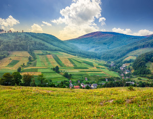 meadow near village in autumn mountains at sunrise