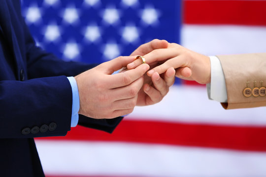 One groom puts ring on another man's finger on American flag background