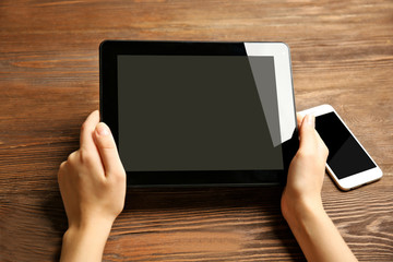 Mobile phone and female hands using tablet, on the wooden background