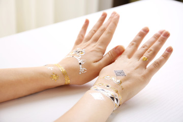 Silver and golden flash tattoo on female hands over white background