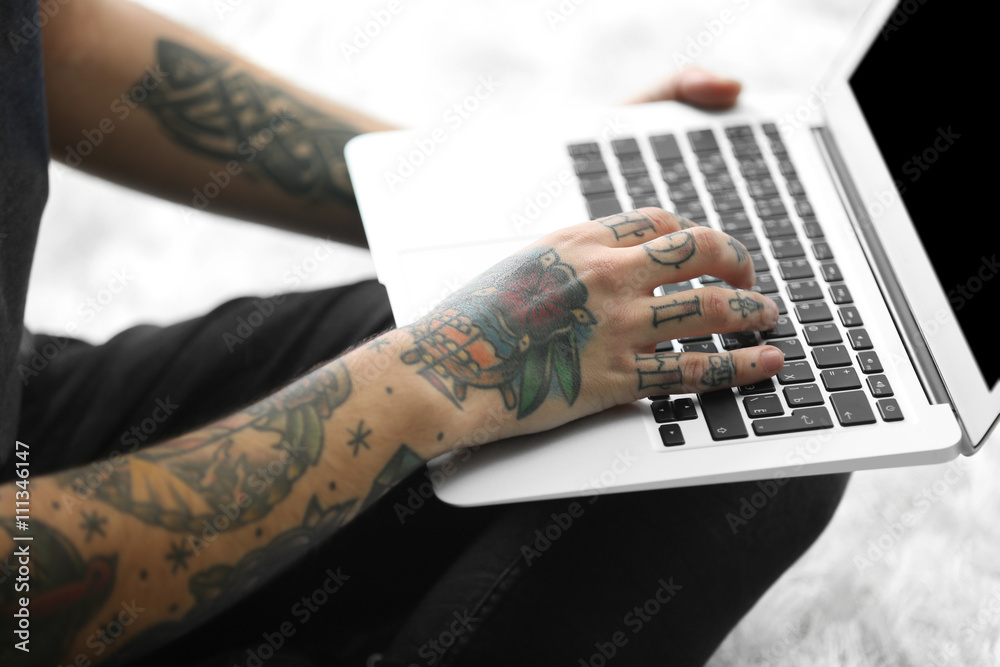 Canvas Prints Young man with tattoo using laptop on a floor at home