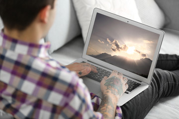 Young man with tattoo using laptop on a sofa at home