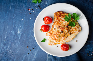 Roasted turkey steak with tomatoes, parsley and spice in white bowl on dark blue background. Selective focus. Toned image