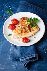 Roasted turkey steak with tomatoes, parsley and spice in white bowl on dark blue background. Selective focus. Toned image