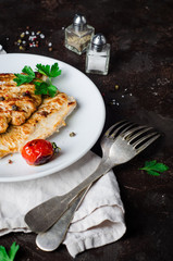 Roasted turkey steak with tomatoes, parsley and spice in white bowl on dark slate background. Selective focus. Toned image