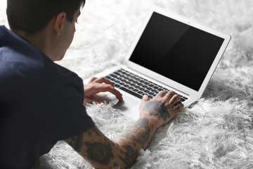 Young man with tattoo using laptop on a floor at home