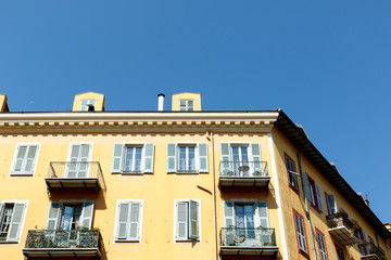 Yellow apartment building in Nice, France, with balconies and a blue sky background. 