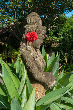 Balinese sculpture with red flower in garden in Ubud, Bali. Indo