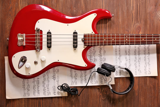 Electric guitar with headphones and notes on wooden background