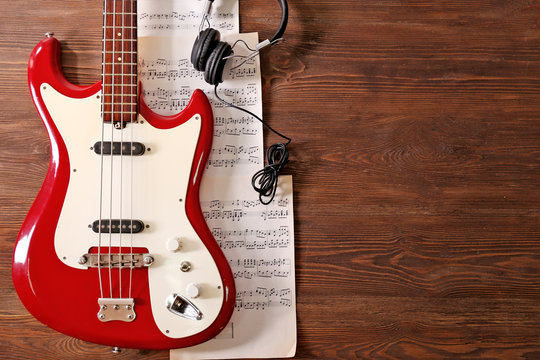 Electric guitar with headphones and notes on wooden background