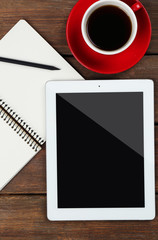 Digital tablet with cup of coffee and notebook on wooden table, closeup