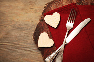 Composition of fork, knife, napkin and decorative hearts on cutting board, on wooden table background
