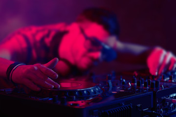 DJ playing music at mixer on colorful blurred background