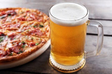 Tasty pizza and glass of beer are on wooden table, close up