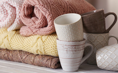Stack of knitted clothes and cups on wooden table indoors