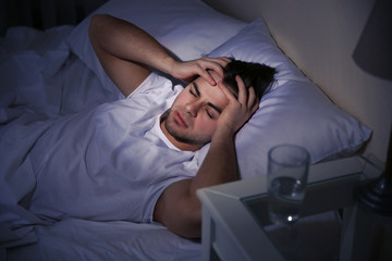 Young man holding his head in bed at night