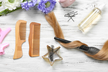 Fototapeta na wymiar Strand of hair with flowers, barber equipment and tools on light wooden background