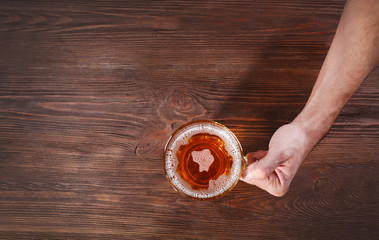 Male hand holding glass of beer on wooden background