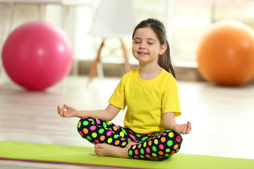 Little cute girl practicing yoga pose on a mat indoor