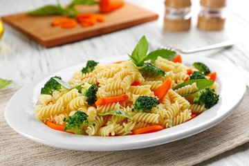 Boiled fusilli pasta with carrot, broccoli and basil on white plate