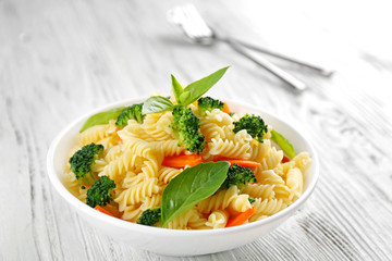 Boiled fusilli pasta with carrot, broccoli and basil on white plate
