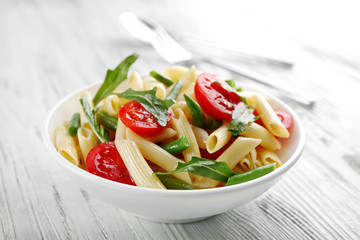 Boiled penne pasta with tomatoes, French bean and arugula on white plate