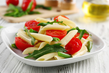 Boiled penne pasta with tomatoes, French bean and arugula on white plate