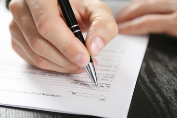 Male hand with pen signing document at the desk closeup