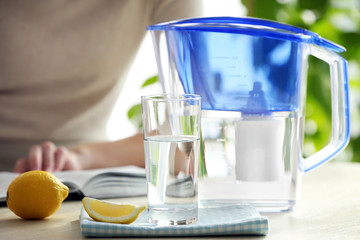 Water filter jug with lemon, glass and reading woman on background