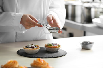 Female hands decorating fruit tarts with sugar powder.