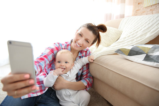 Young mother taking a selfie with her baby near the couch, close up