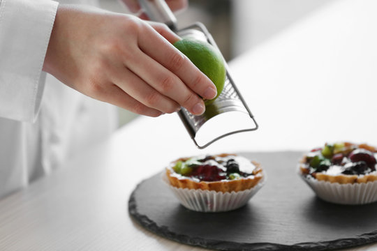 Female hands decorating fruit tarts with lime zest