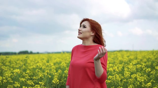Pretty red girl standing with a rape-flower field in the background, smiling 4K