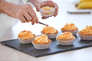Male hands decorating tarts with sugar balls.
