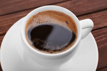 Cup of coffee with brown foam on wooden background, close up
